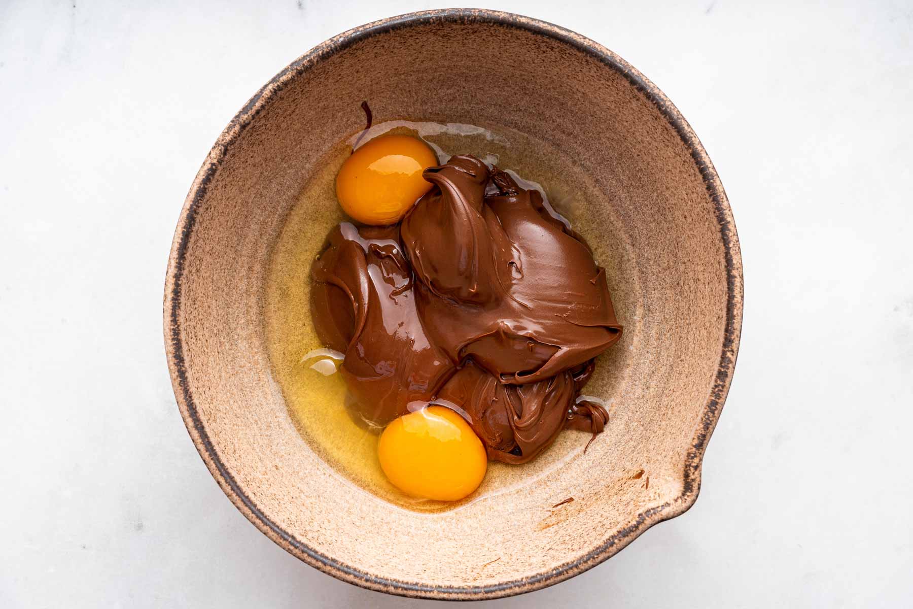 Brown bowl with chocolate mixture and two cracked eggs.