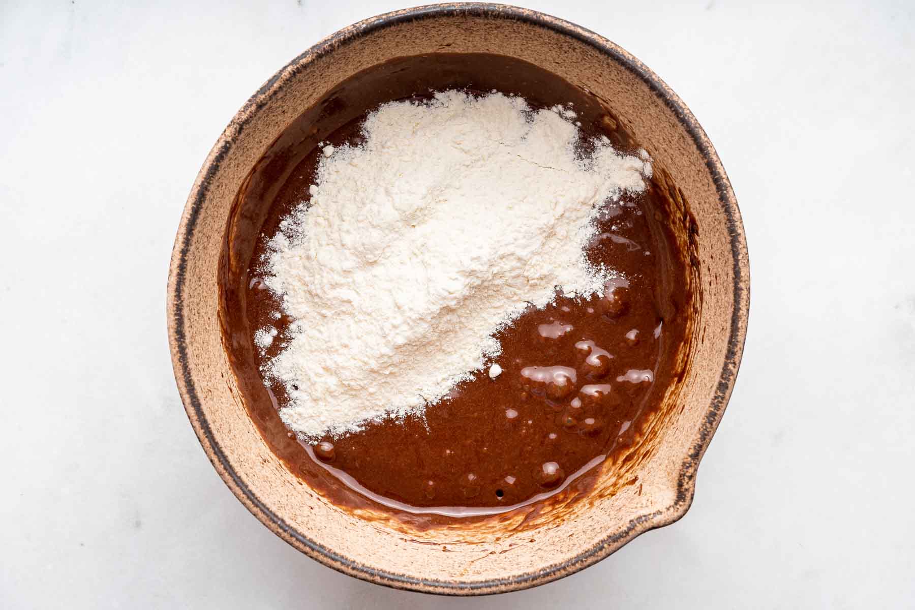Chocolate mixture in brown bowl with flour sprinkled on top.