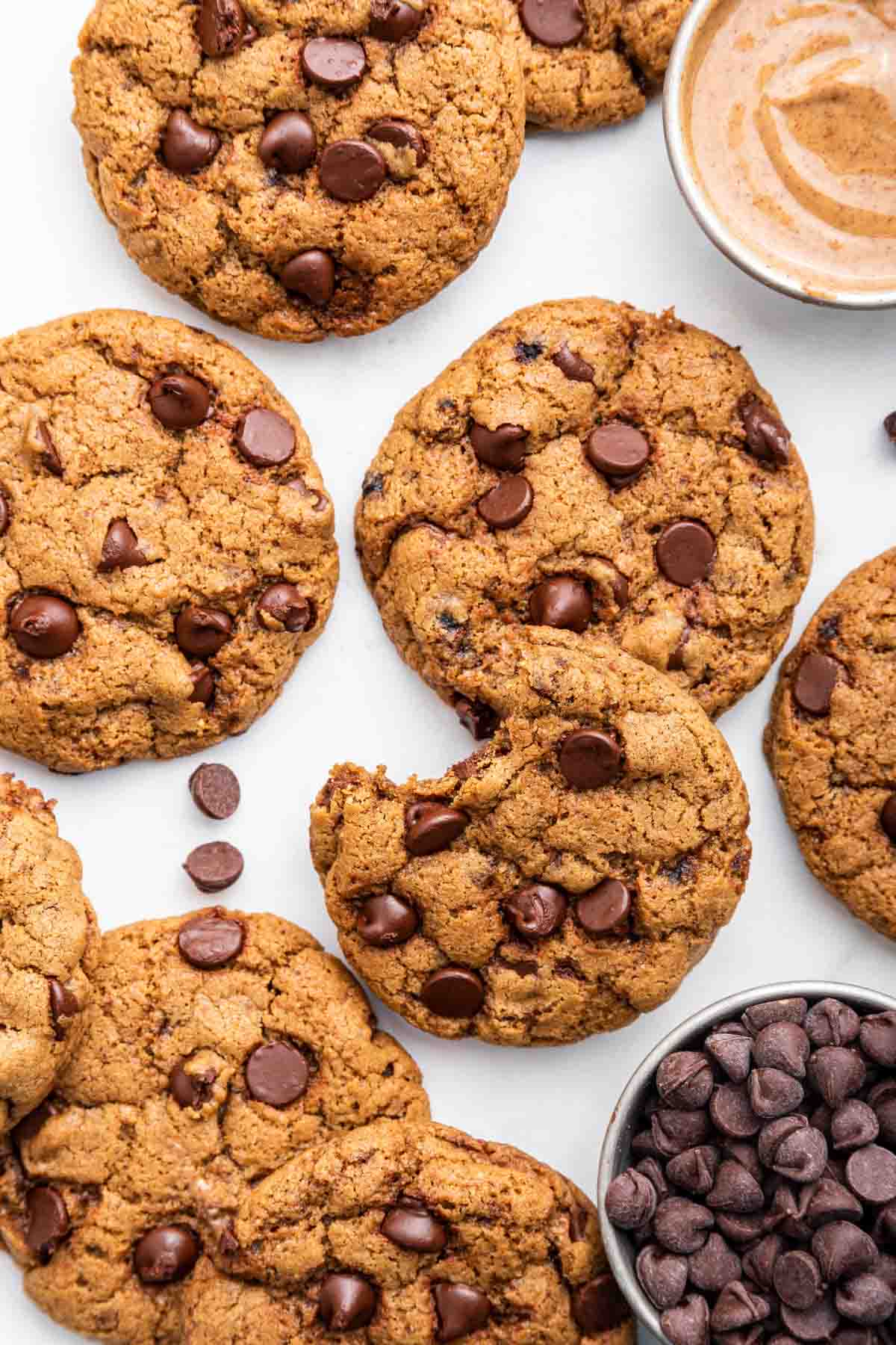 Almond butter chocolate chip cookies spread on a white counter with a. bowl of almond butter.