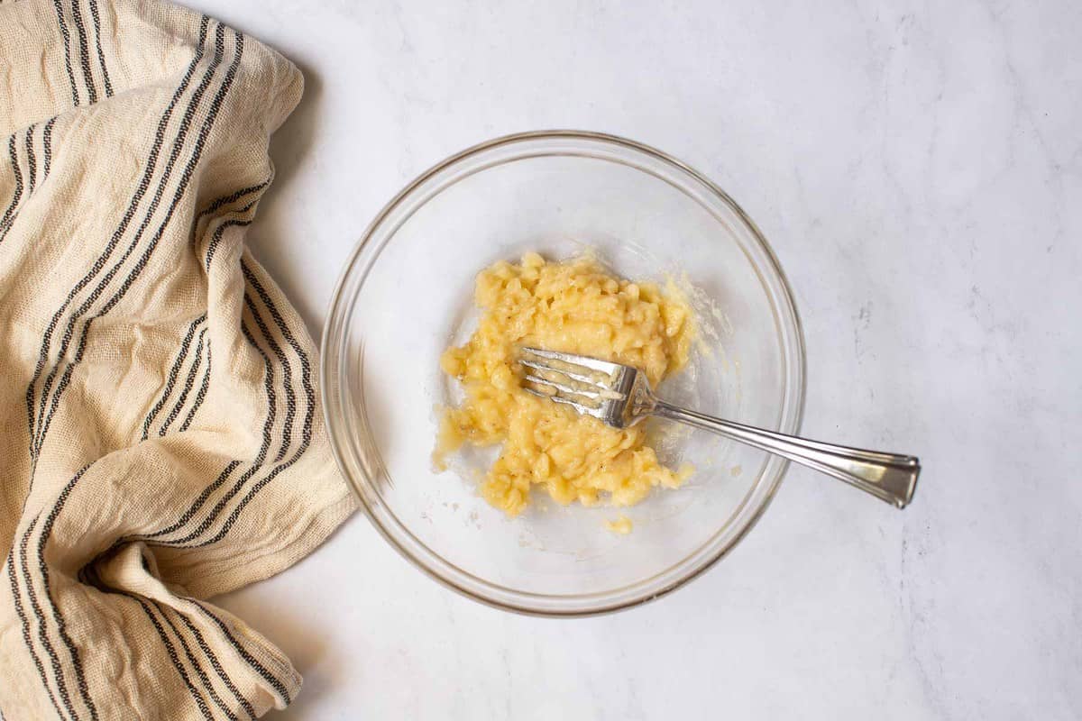 One banana, mashed in a bowl with a fork.