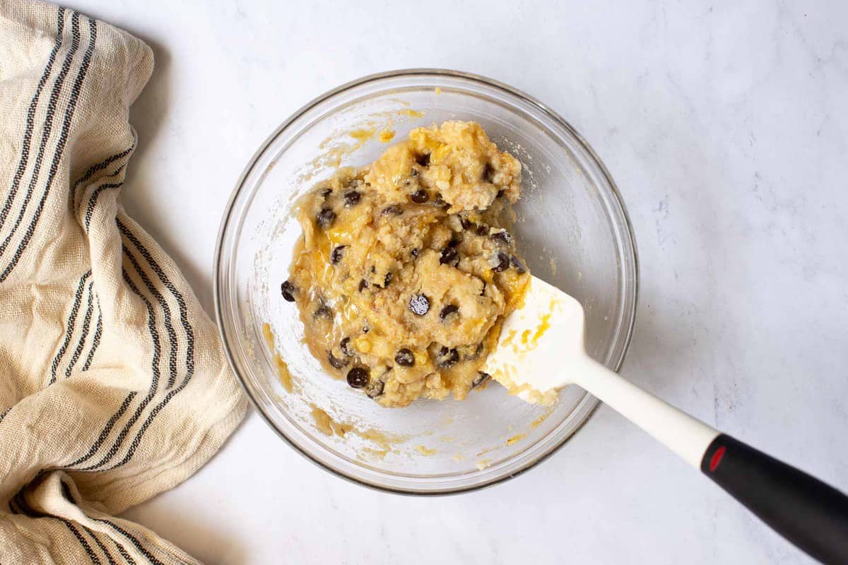 Banana muffin batter in a clear bowl with spatula.