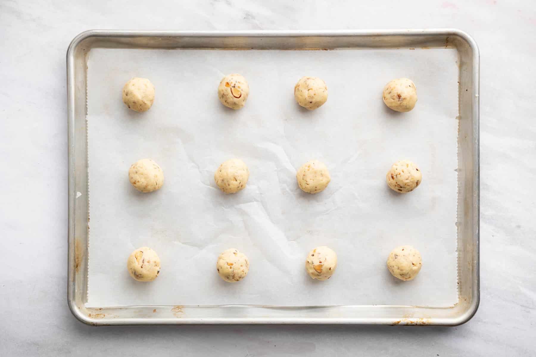 One dozen small yellow dough balls on a cookie sheet lined with parchment.