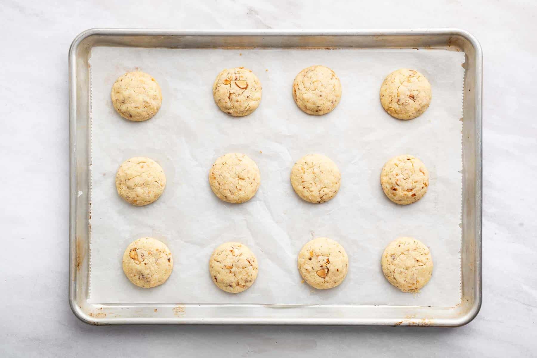 One dozen almond snowball cookies on a cookie sheet.
