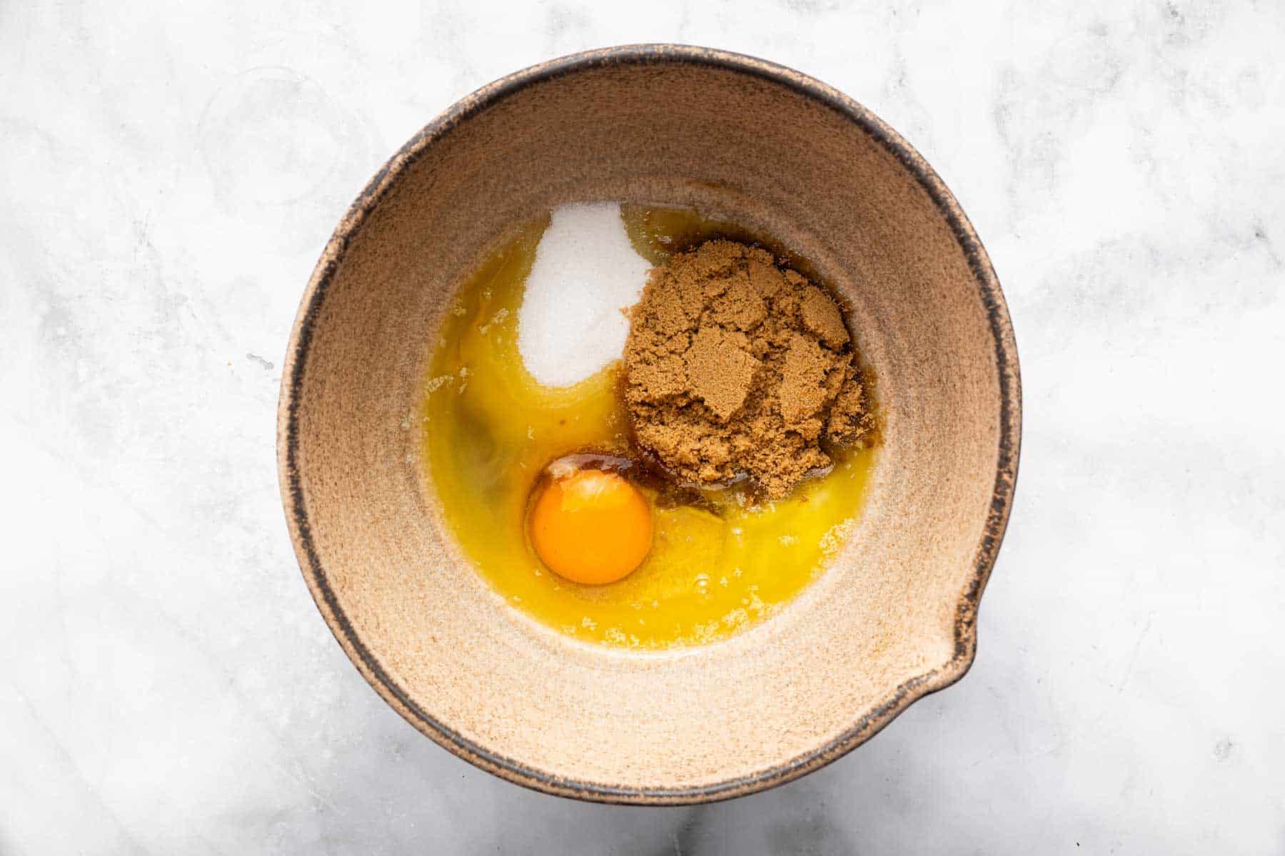 Brown bowl with sugars, egg, and melted butter.