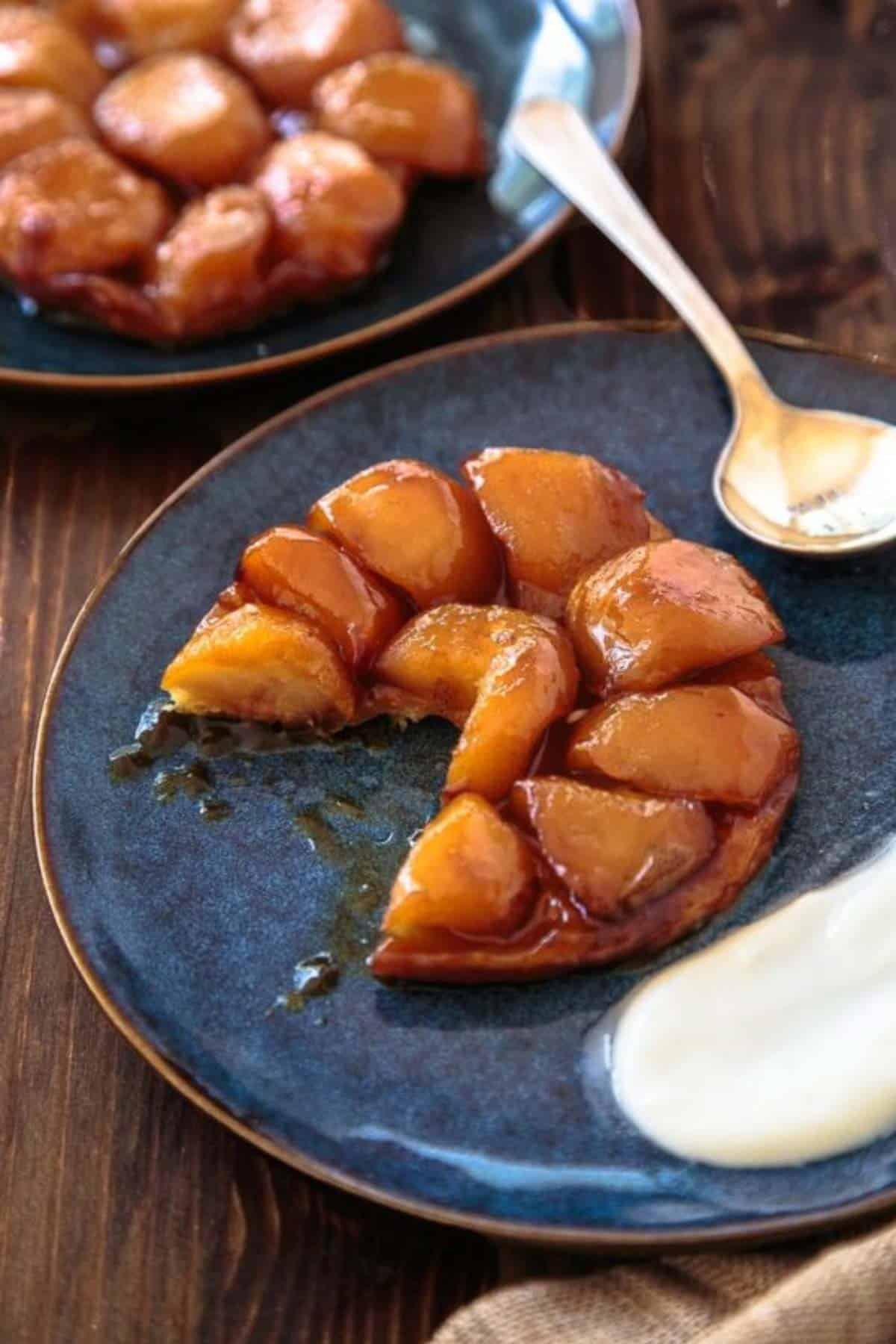 Two servings of apple tarte tatin on dark blue plates with cream dollop.