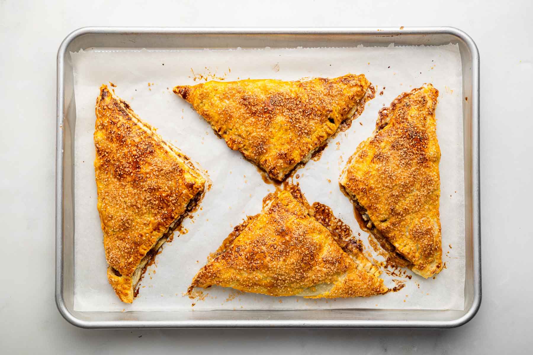 Four triangle apple turnovers on a baking sheet.