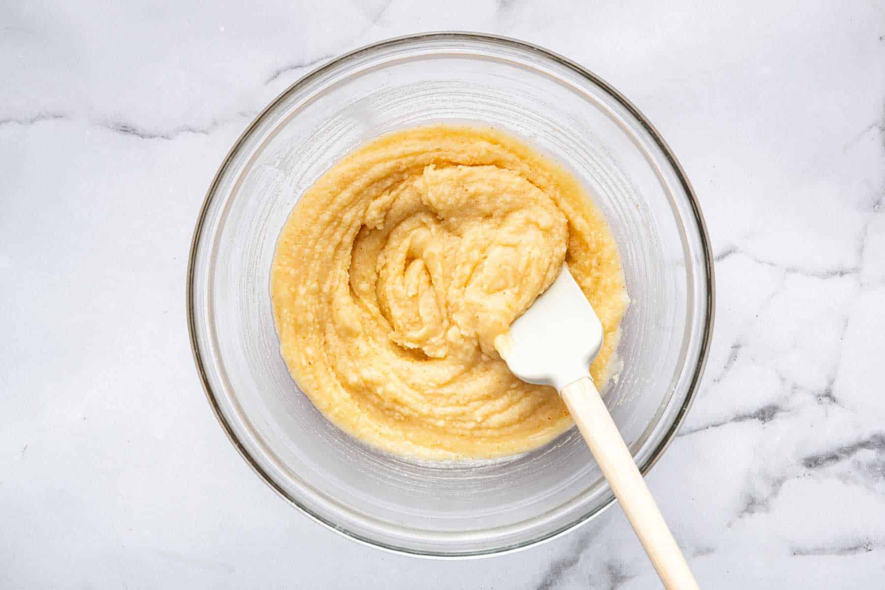 Clear bowl with bright yellow dessert batter and white spatula.