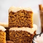 Two square brown slices of applesauce cake with tan frosting stacked.