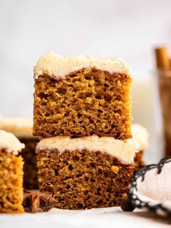 Two square brown slices of applesauce cake with tan frosting stacked.
