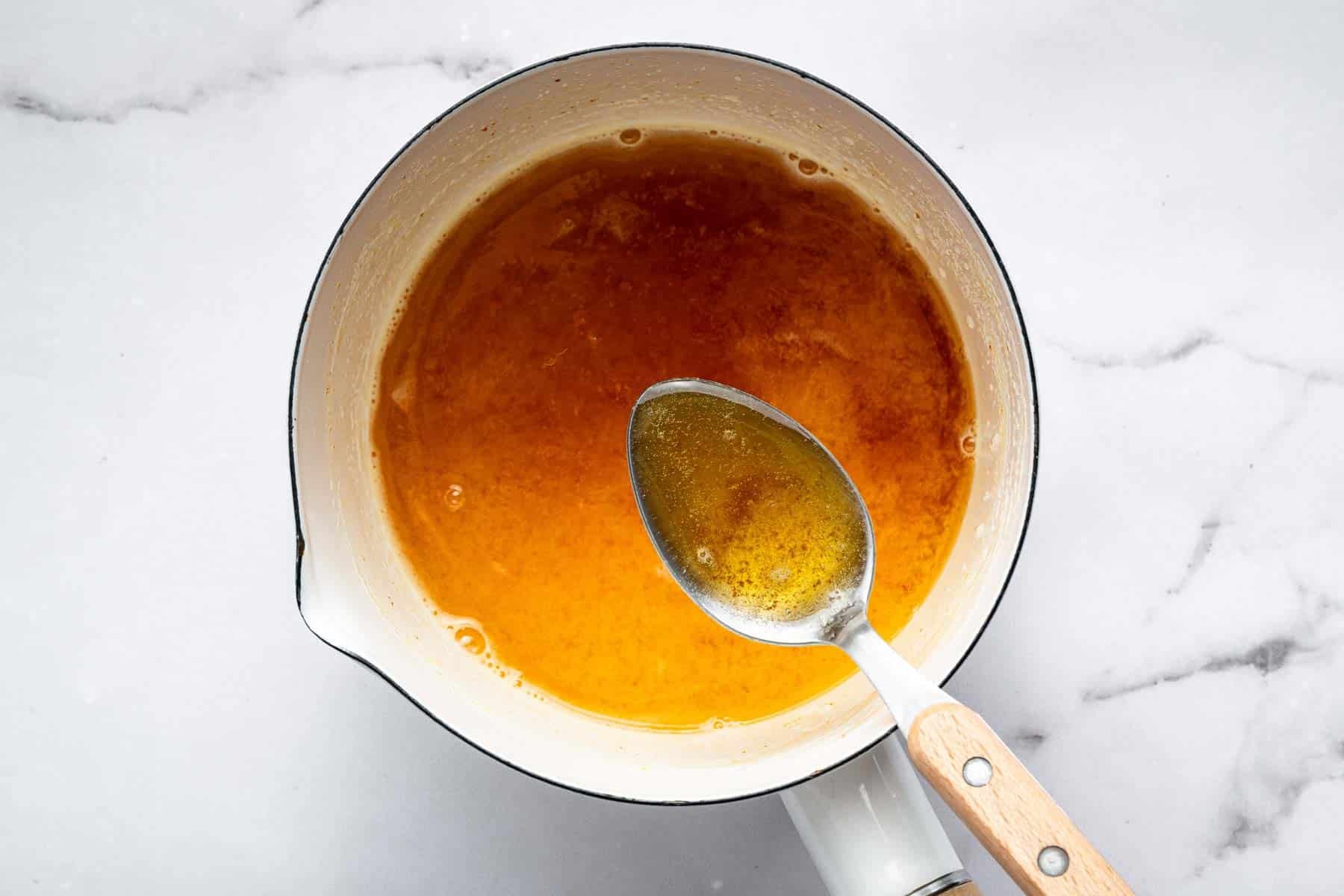 Browned butter in a white saucepan with metal spoon.