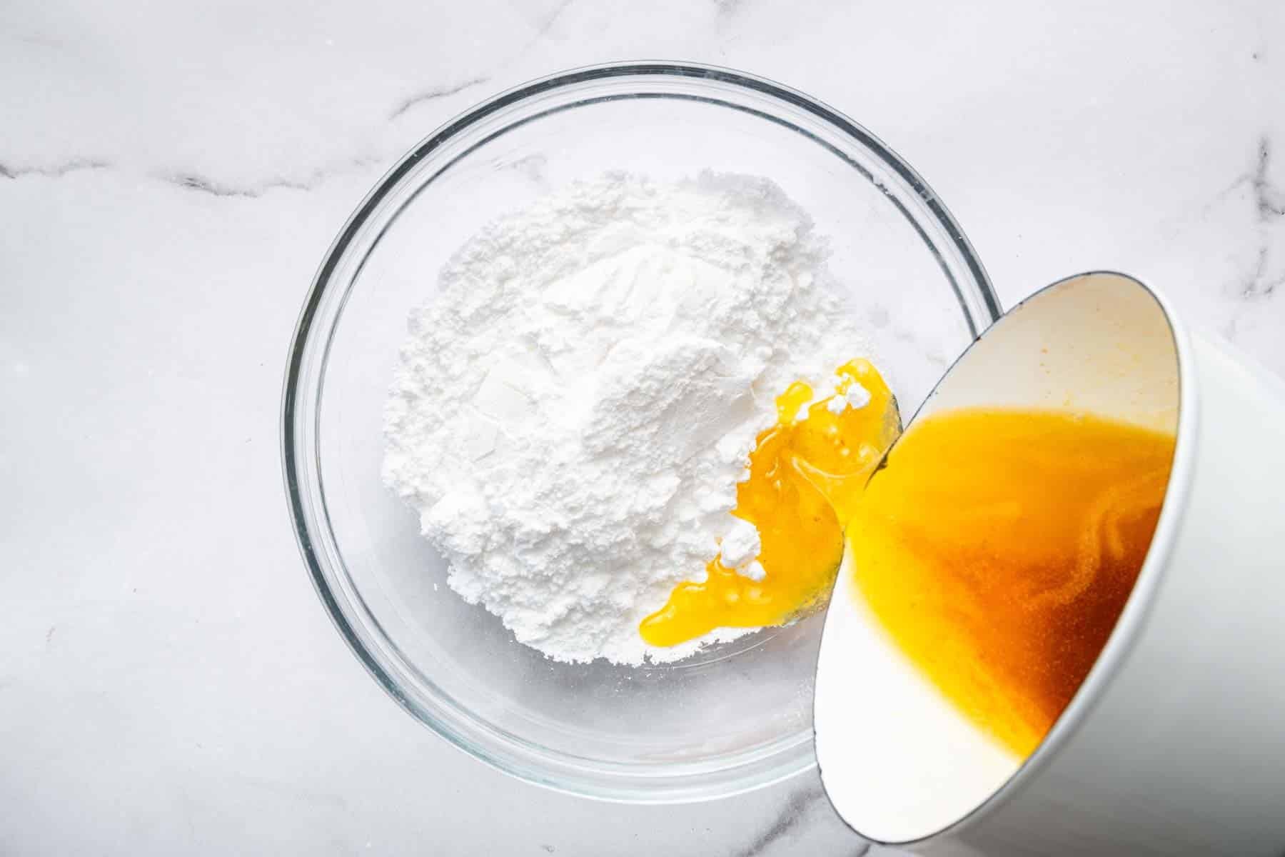 Hand pouring brown butter in a bowl of powdered sugar.