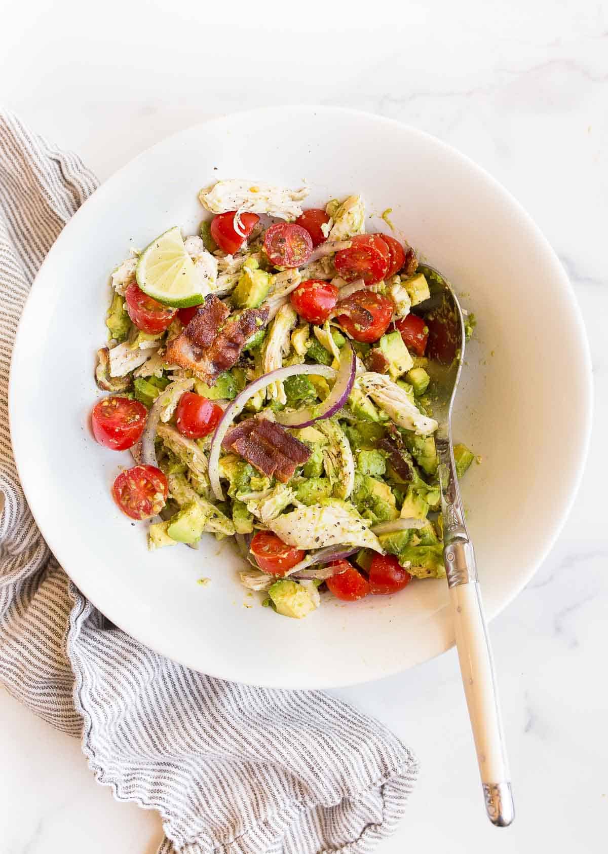 avocado chicken tomato salad in a white bowl with a spoon