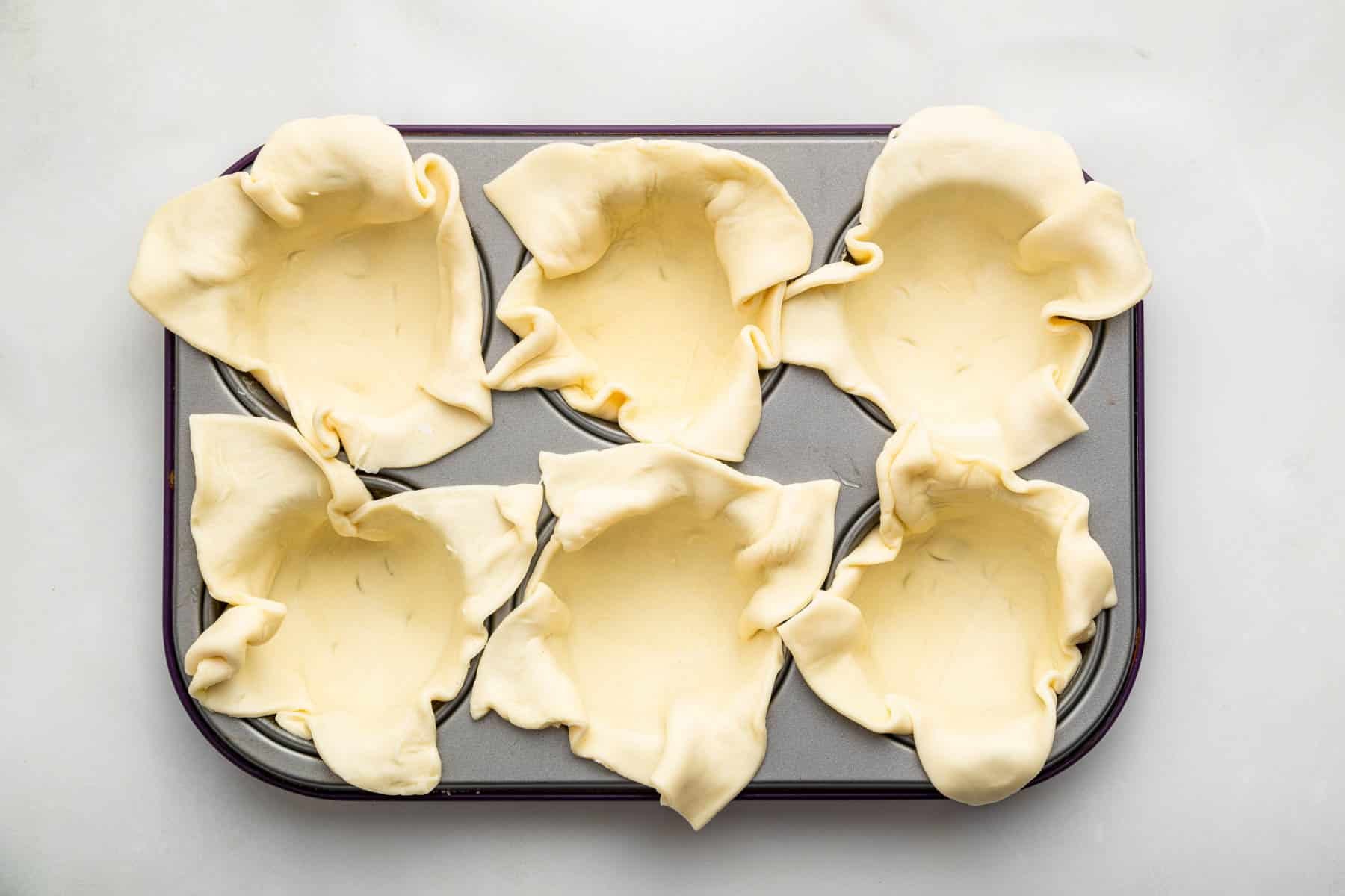 Six muffin cups lined with raw puff pastry dough.