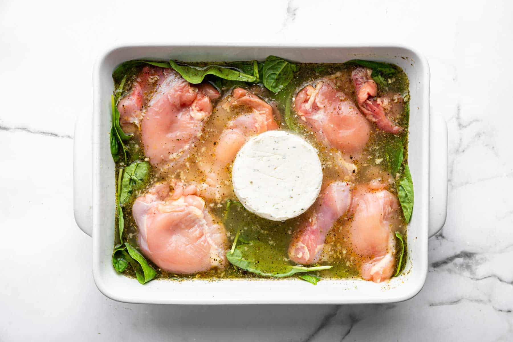 Chicken thighs on a bed of spinach with round white cheese in the center.