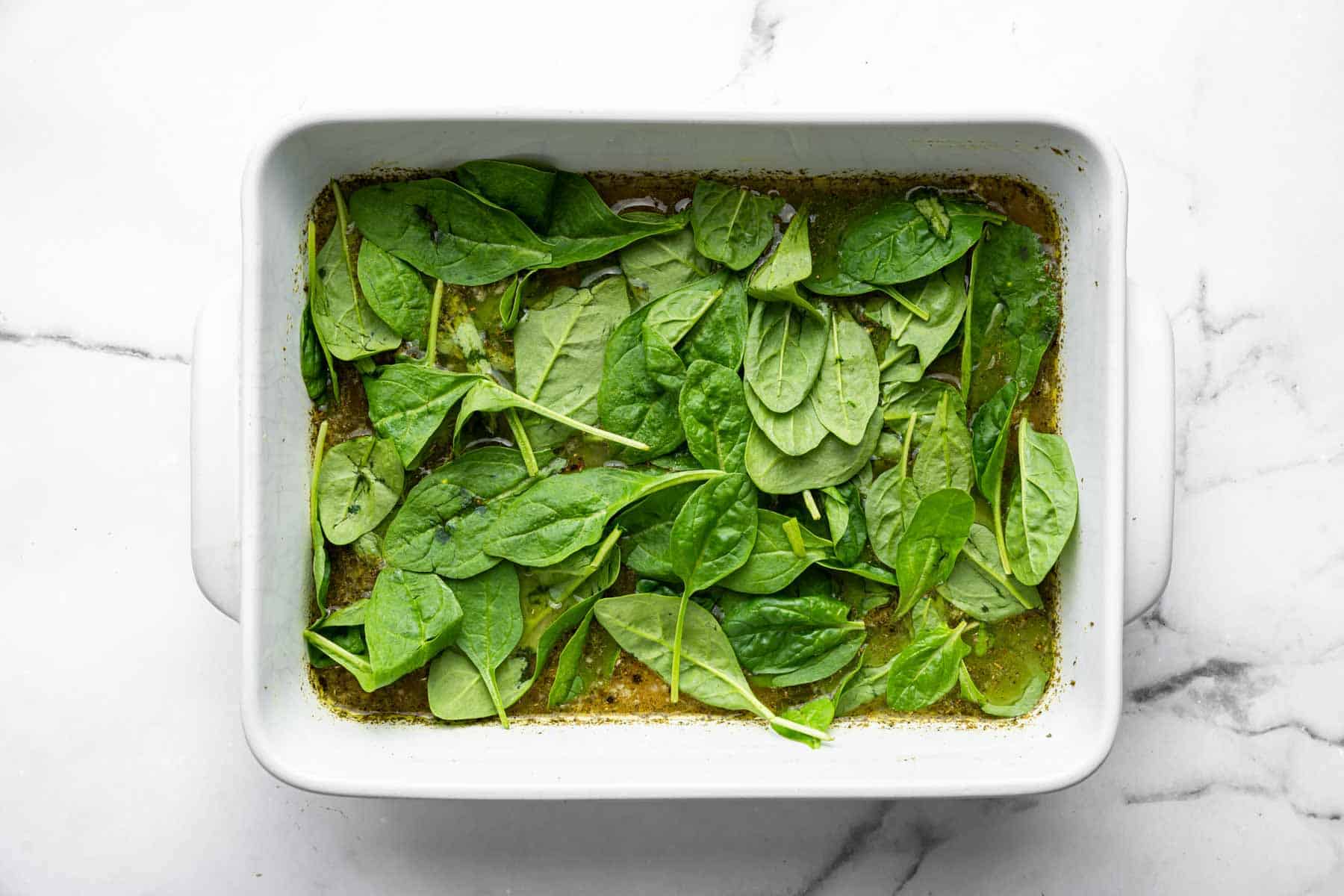 Fresh baby spinach in a white rectangular baking dish.