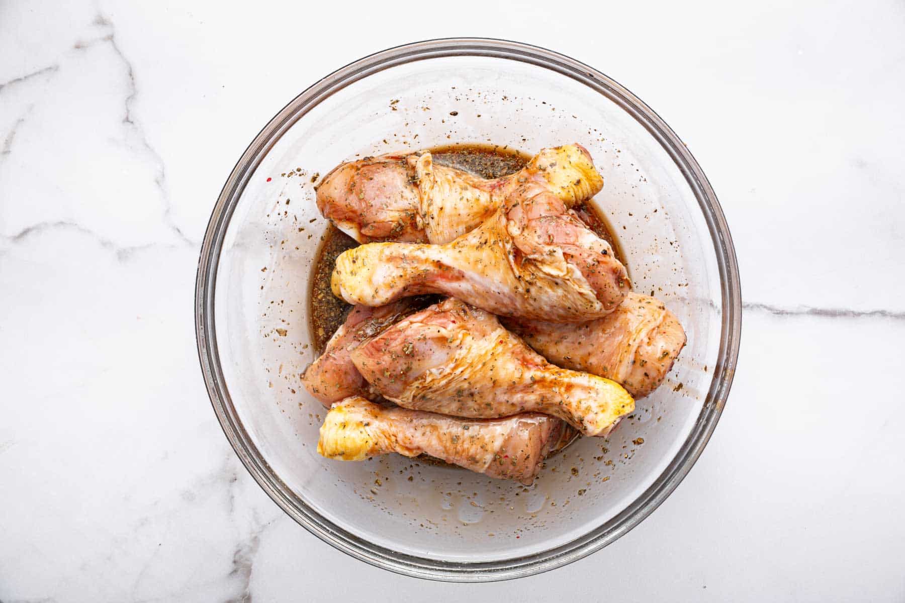 Raw drumsticks with brown marinade on top in bowl.