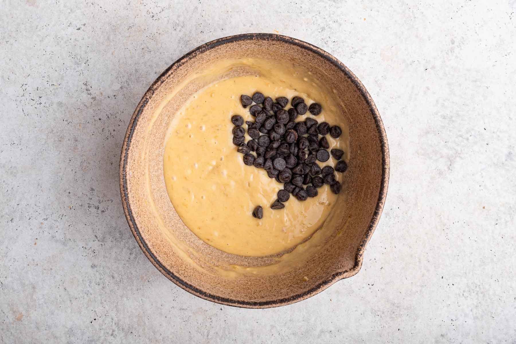 Stirring chocolate chips into yellow batter in a brown bowl.