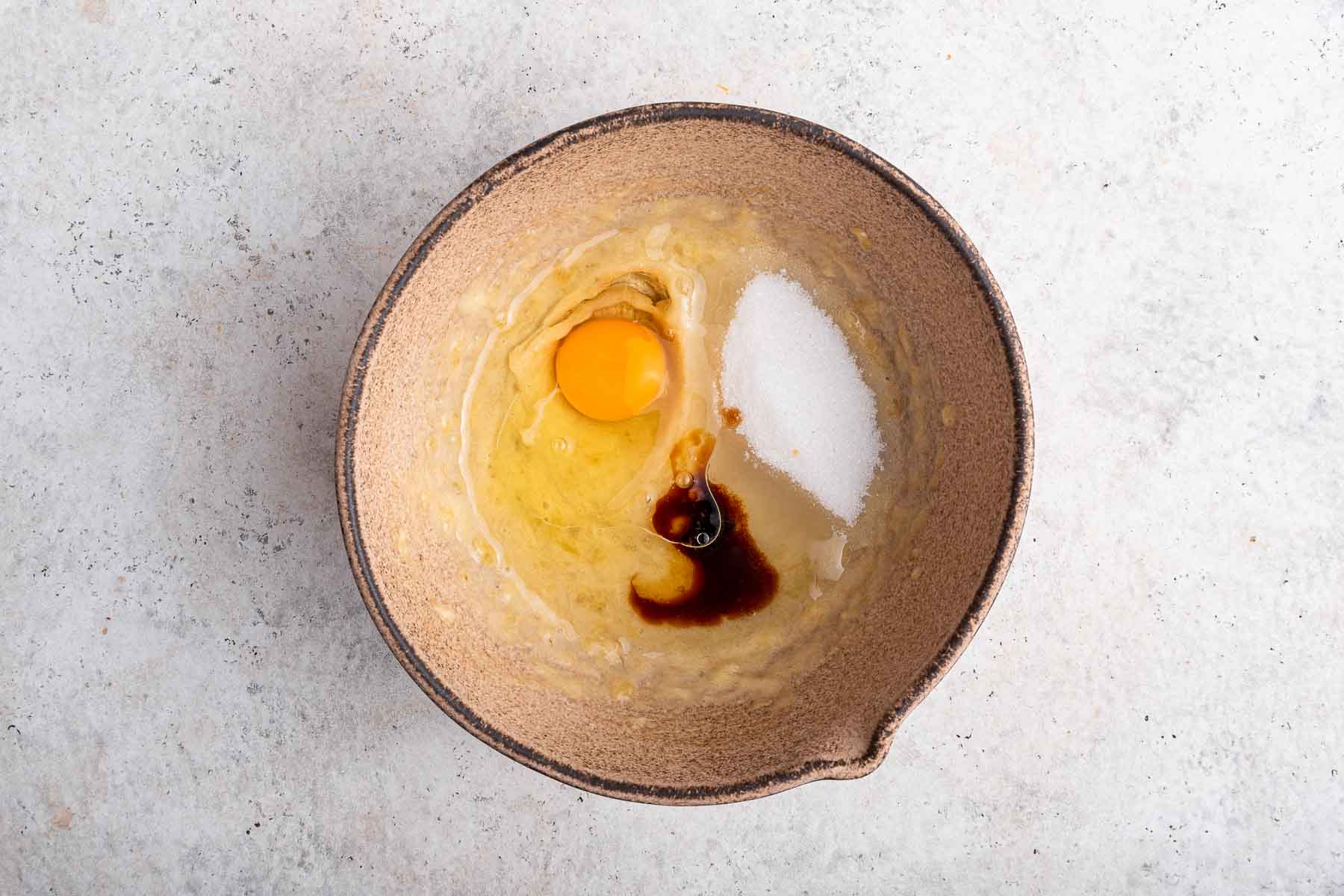 Egg, sugar and vanilla in brown mixing bowl.