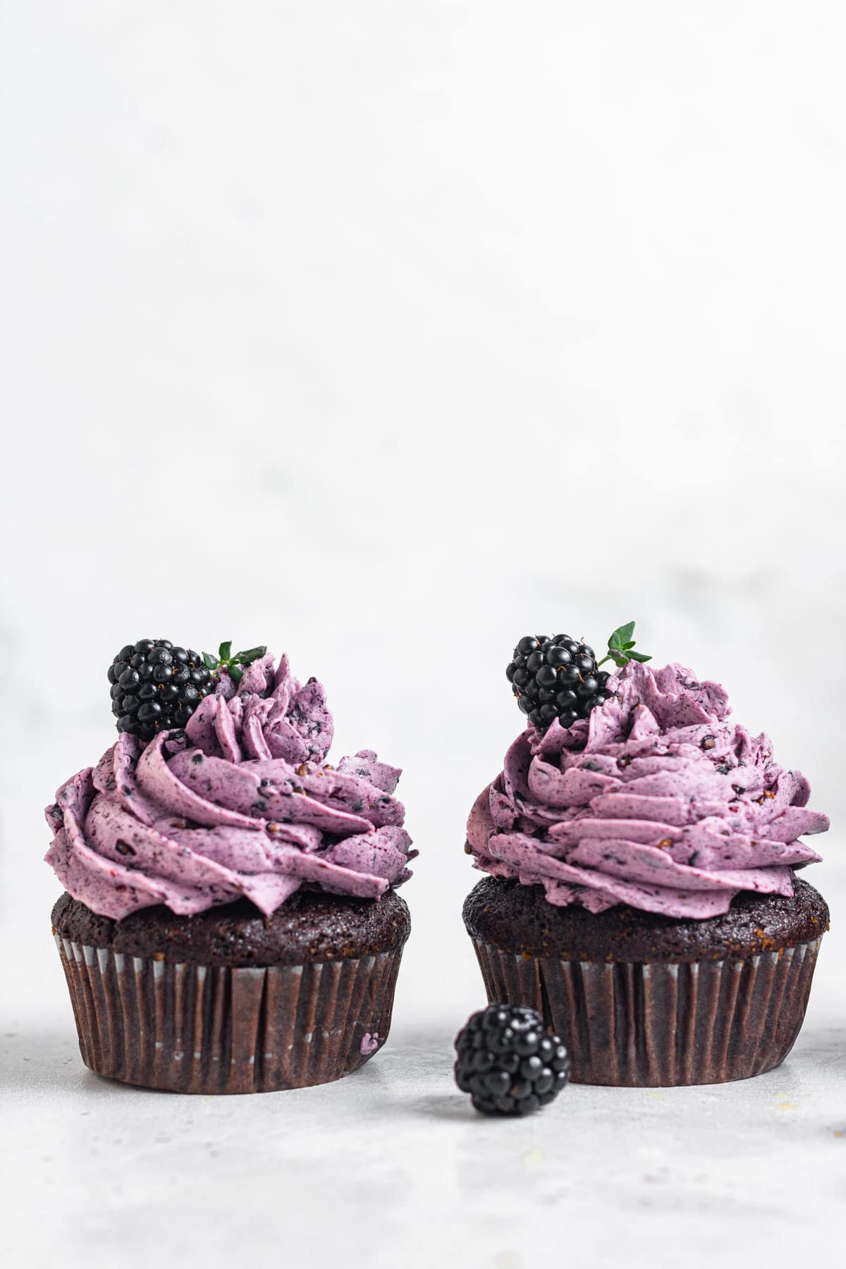 Two chocolate cupcakes with purple frosting and fresh blackberries.