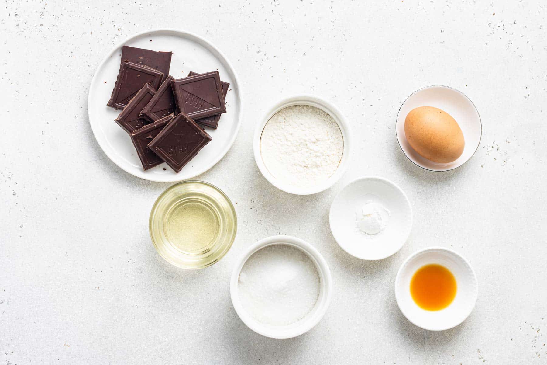Ingredients to make a small batch of chocolate cupcakes on white table.