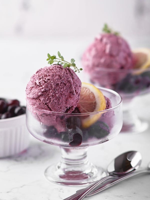 Two glass bowls of blueberry sherbet with lemon and thyme sprig.