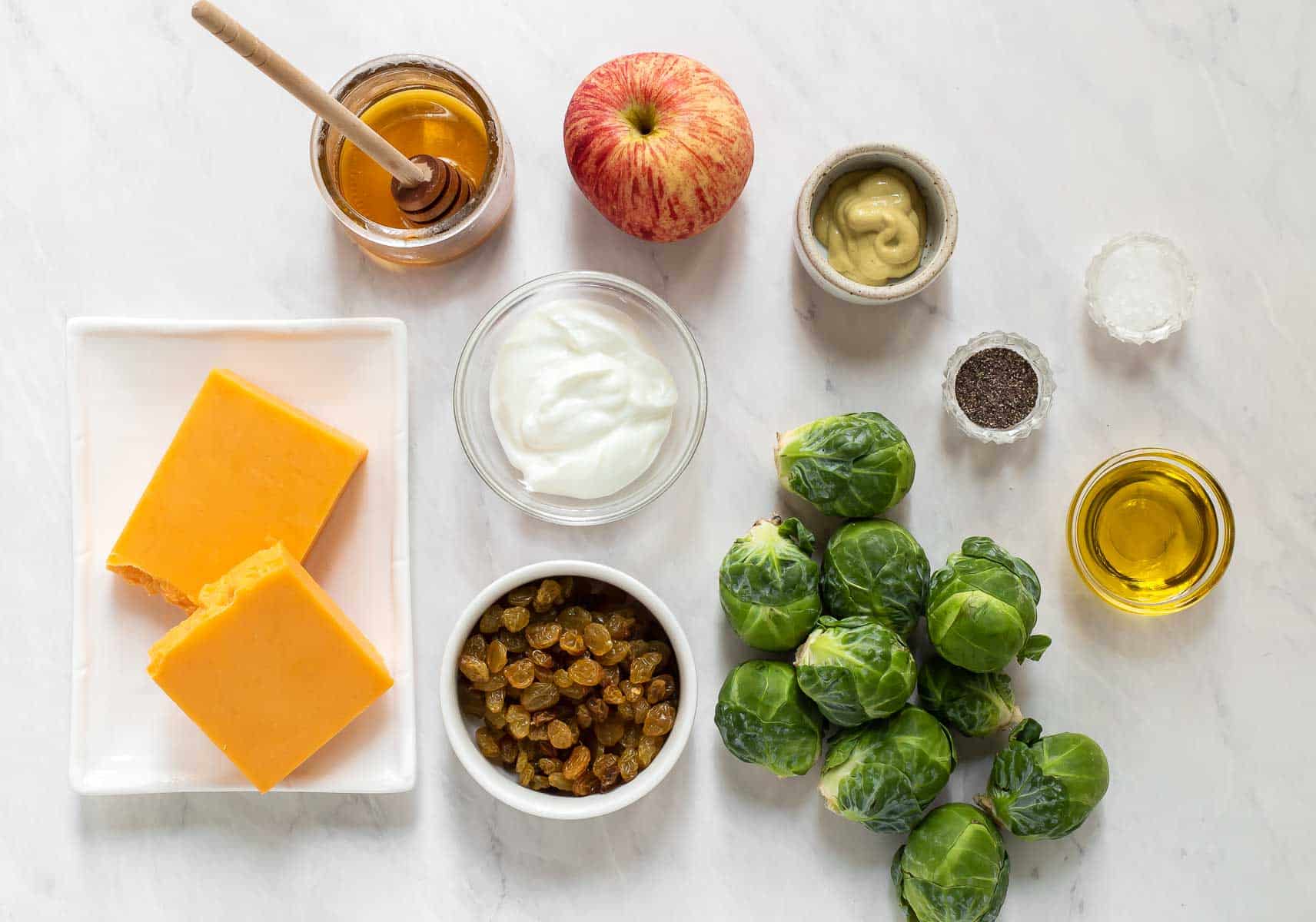 Ingredients for brussels sprout cole slaw on white table.