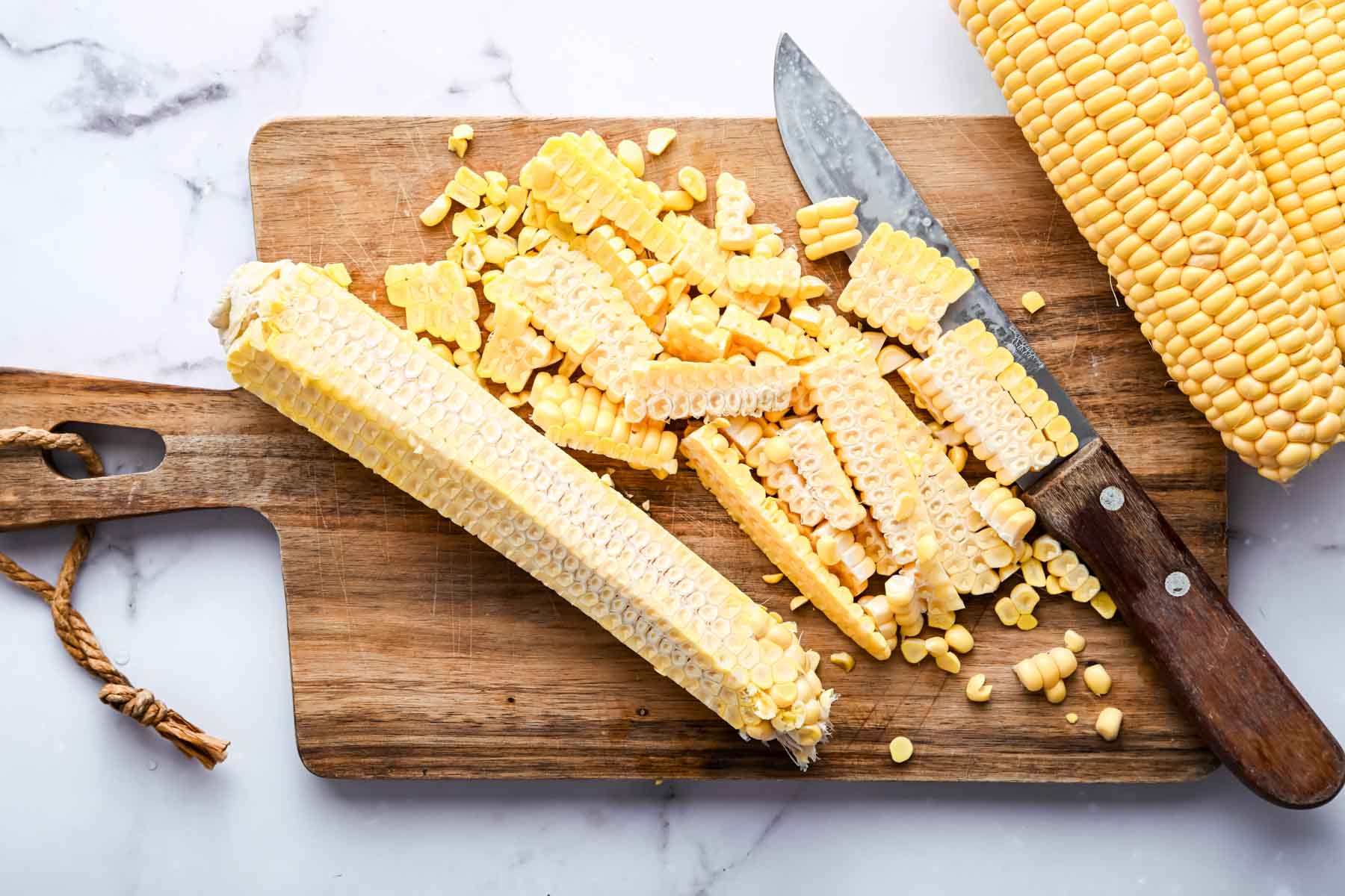 Corn on a cutting board with all of its kernels cut off.