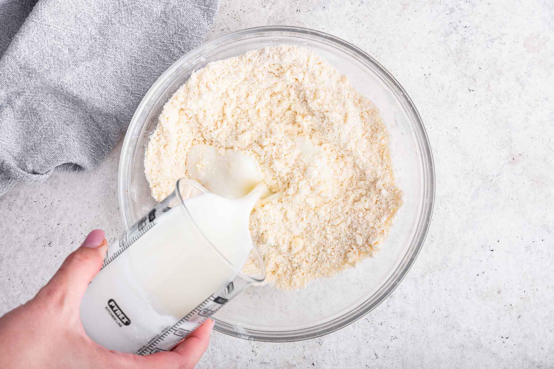 Pouring buttermilk into homemade buttermilk biscuits dough.
