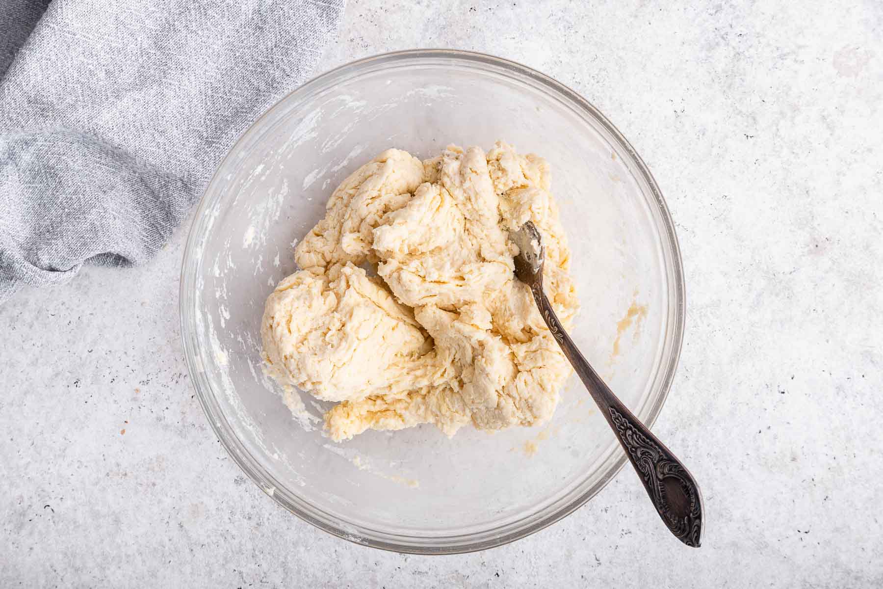 Buttermilk biscuit dough in clear bowl with fork.