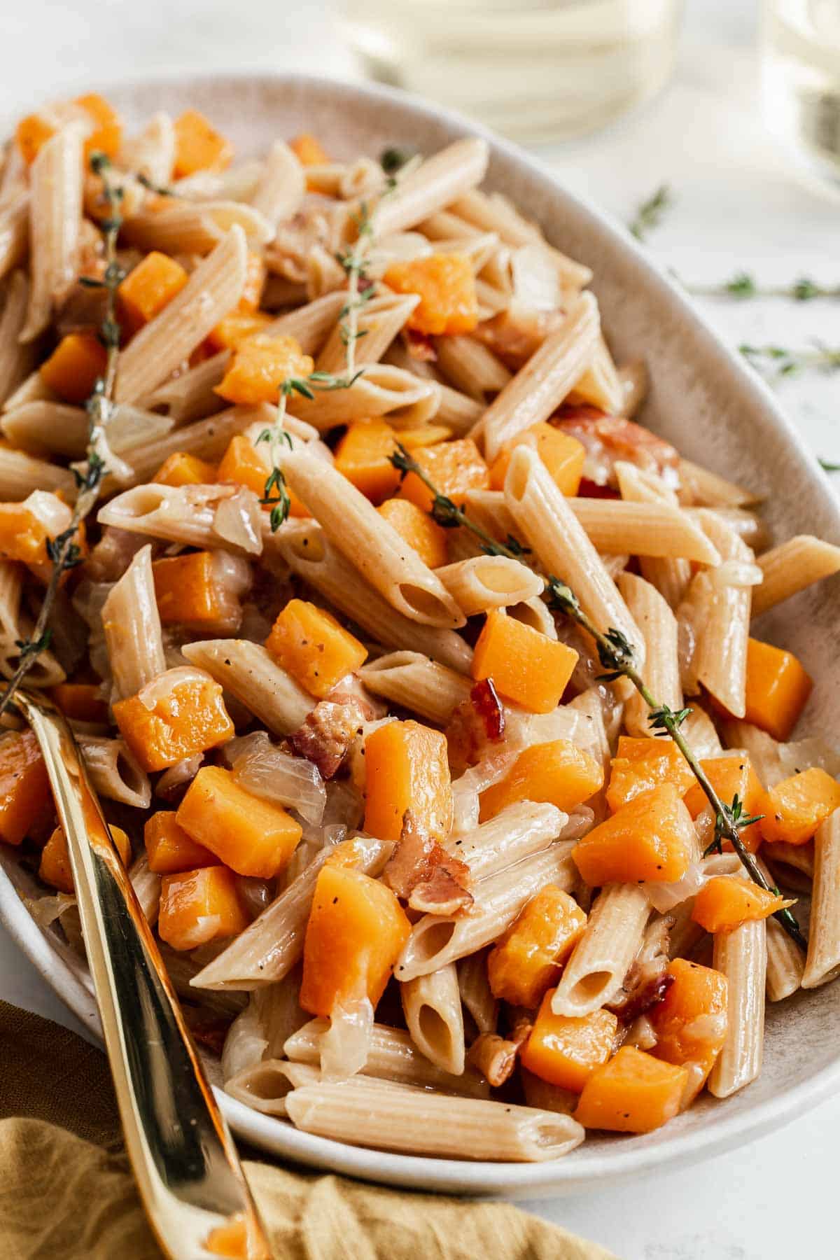 Butternut squash penne pasta on a serving plate with fresh thyme.
