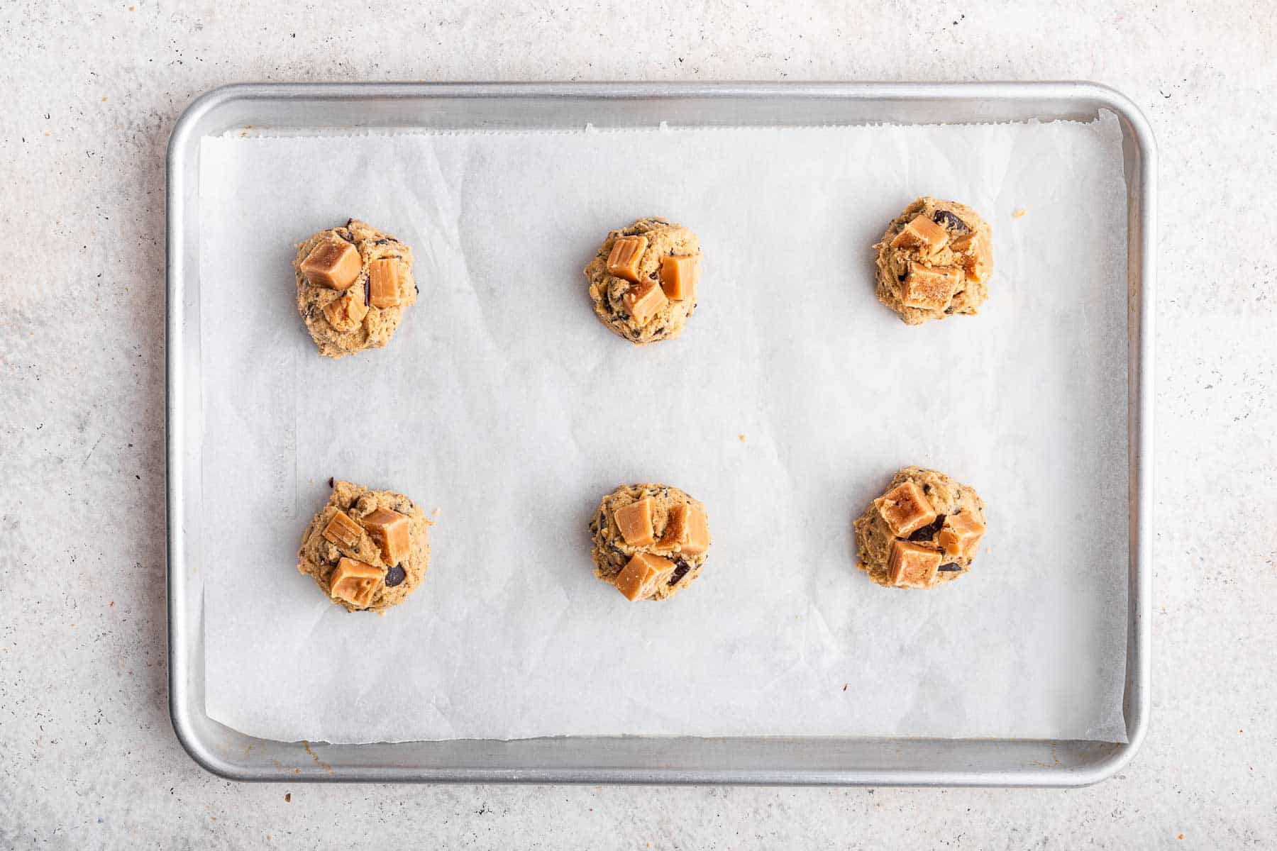 Adding three pieces of chopped caramel on raw cookie dough.