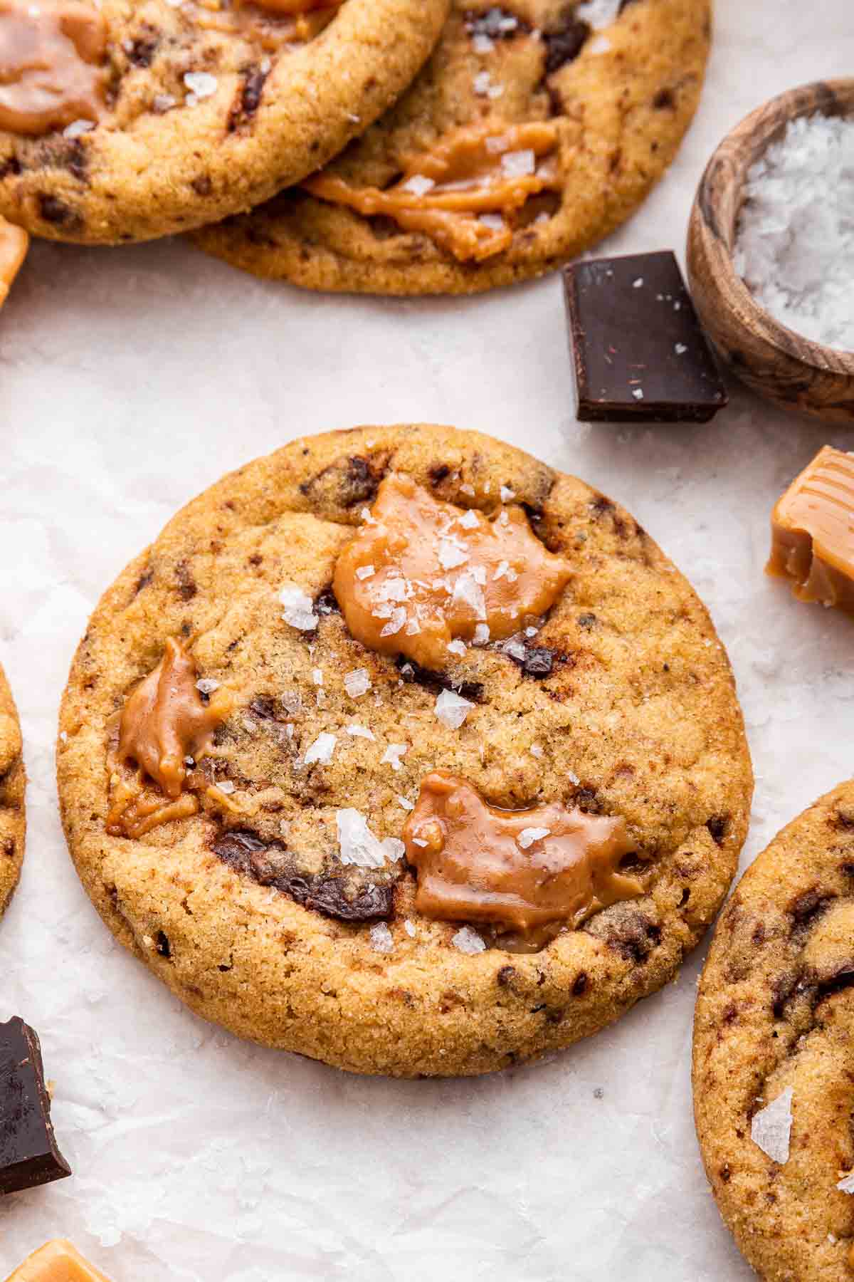 Caramel chocolate chip cookie on surface with big flaky sea salt sprinkled on top.