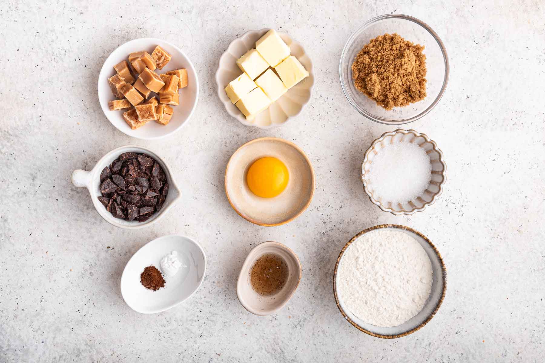 Nine little bowls of ingredients on a marble surface.