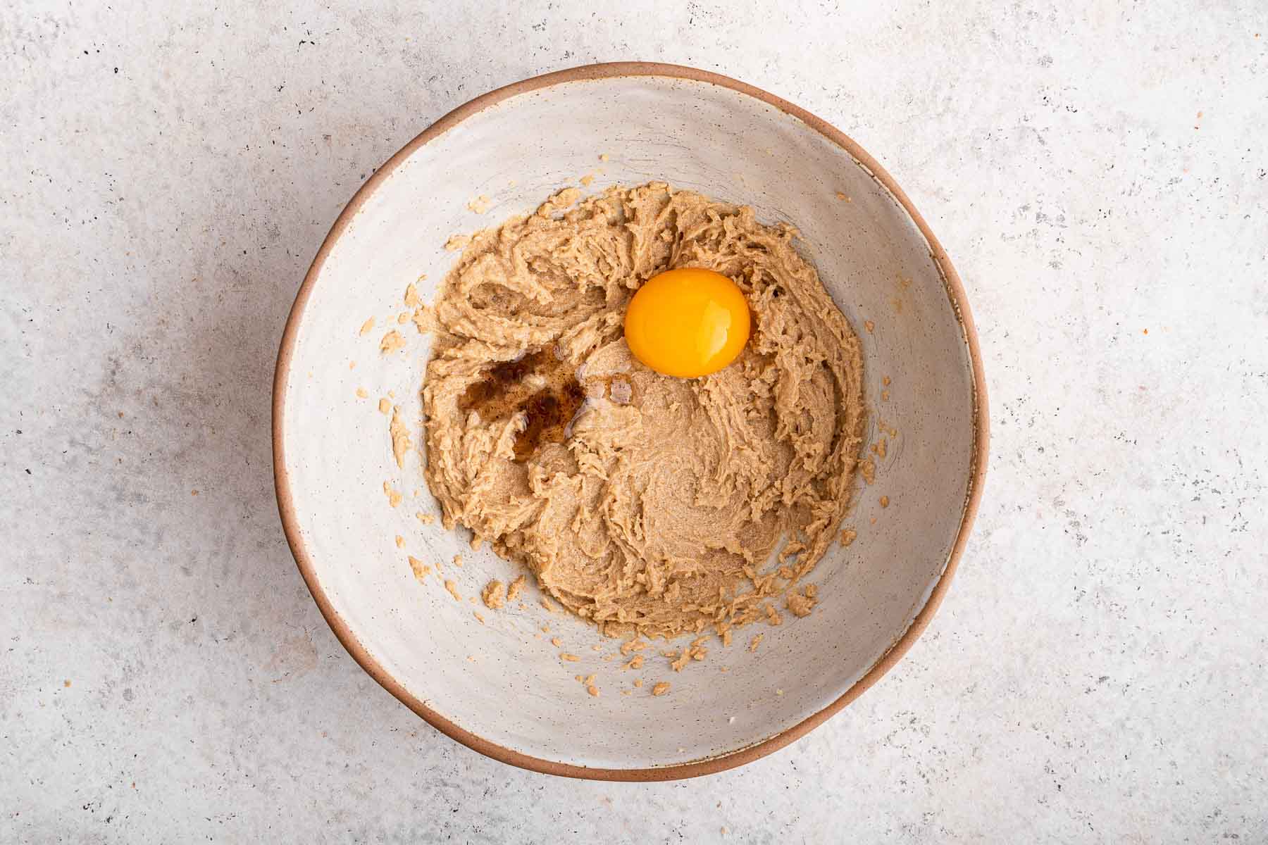 Egg yolk and vanilla on top of brown cookie dough in white bowl.