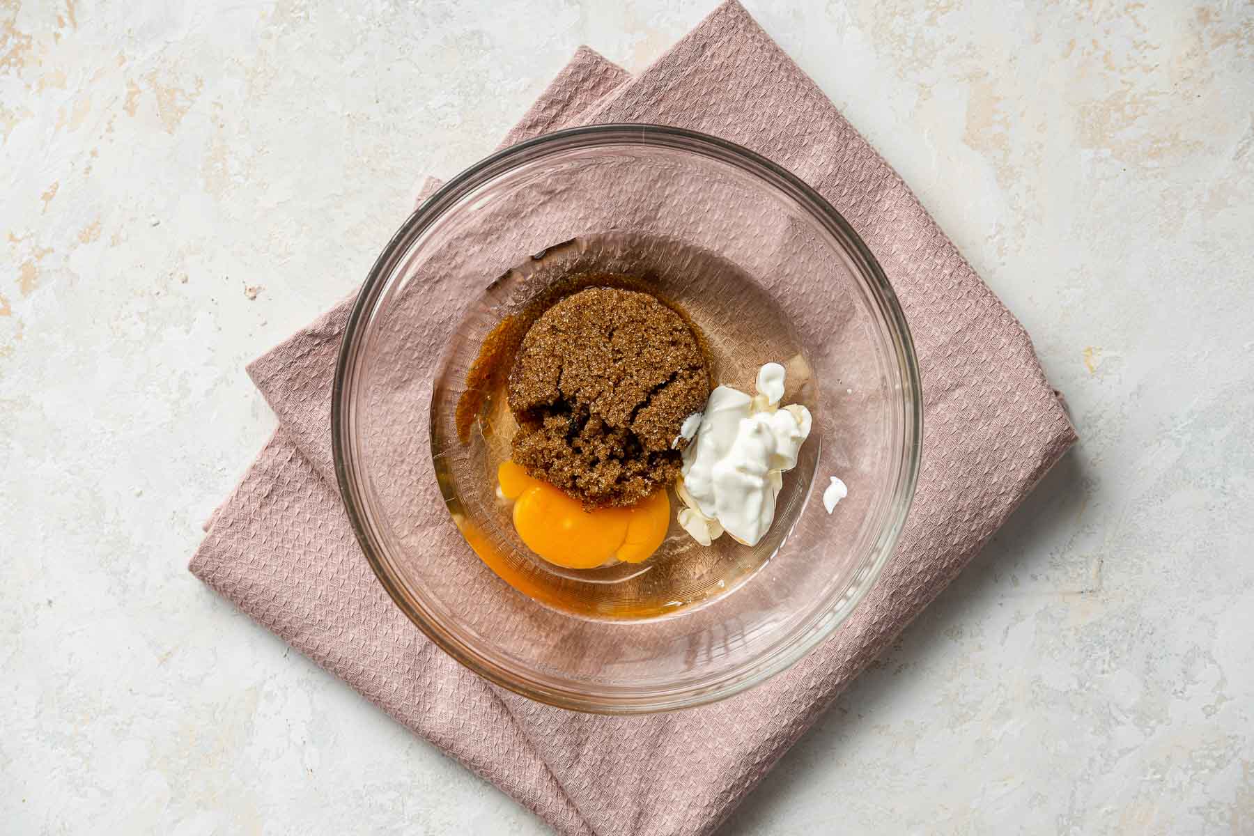 Brown sugar, egg, oil and sour cream in a clear glass bowl.