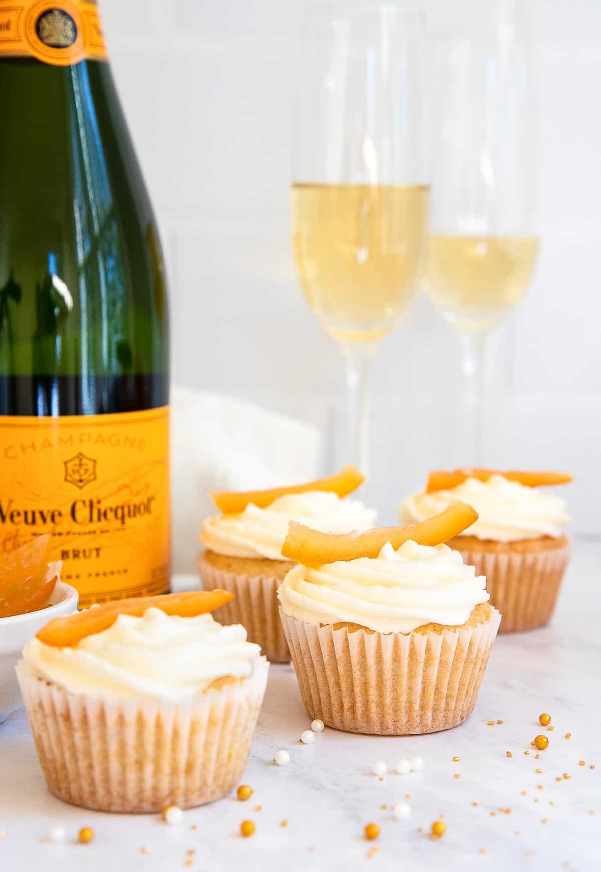 Champagne cupcakes with orange zest on top and bottle of champagne.