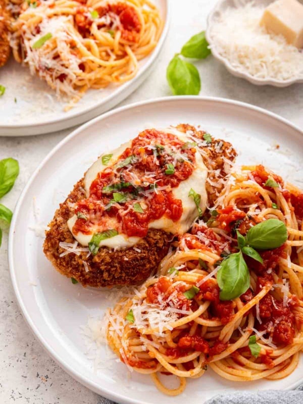 Two plates of chicken parmesan garnished with fresh basil leaves.
