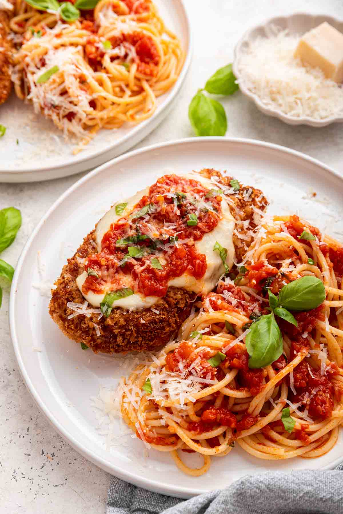 Two plates of chicken parmesan garnished with fresh basil leaves.