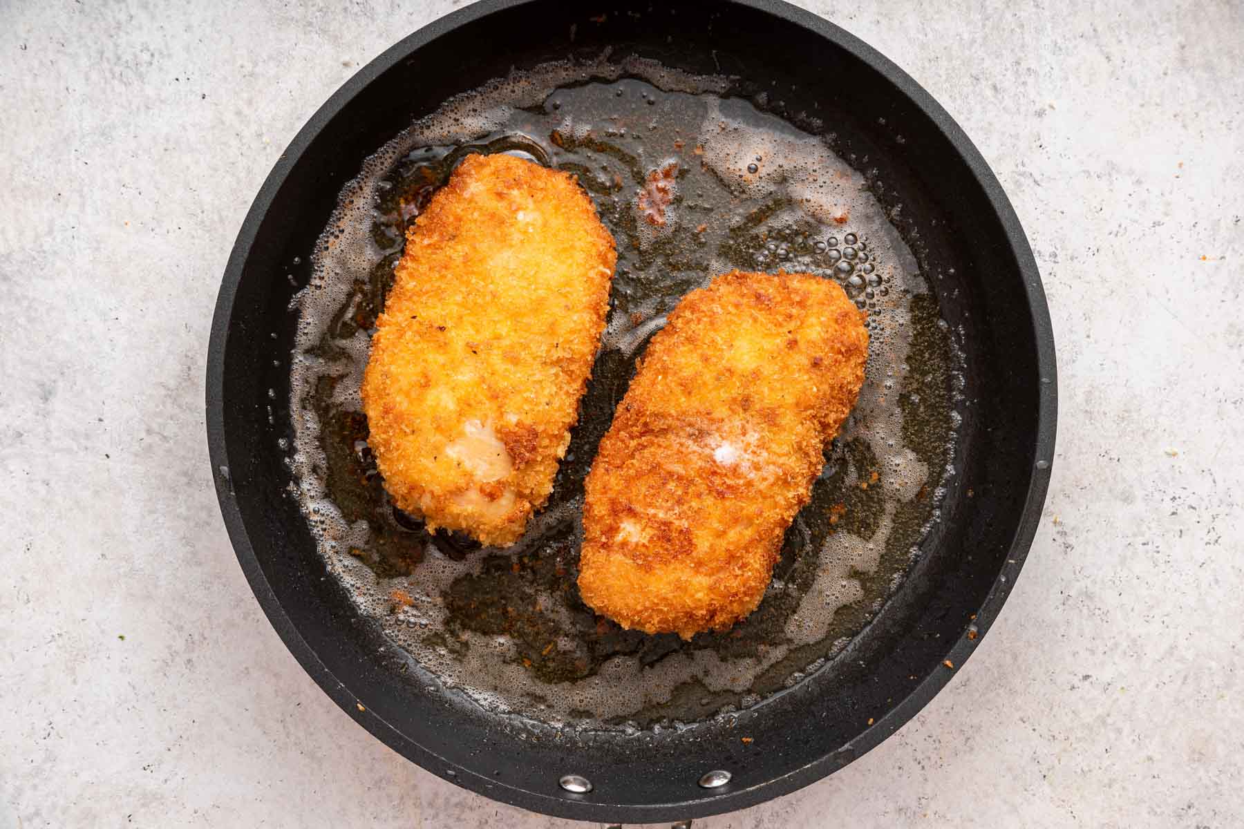 Two rectangular pieces of protein in a skillet with a golden brown crust.