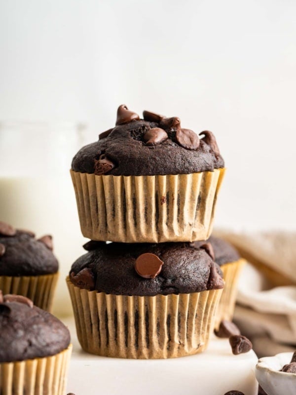 Two chocolate banana muffins stacked on top of each other in brown wrappers.