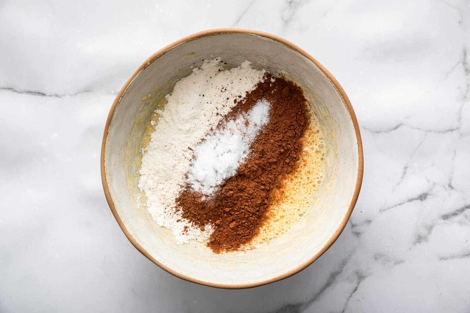 Flour and cocoa powder sprinkled evenly on a bowl of yellow batter.