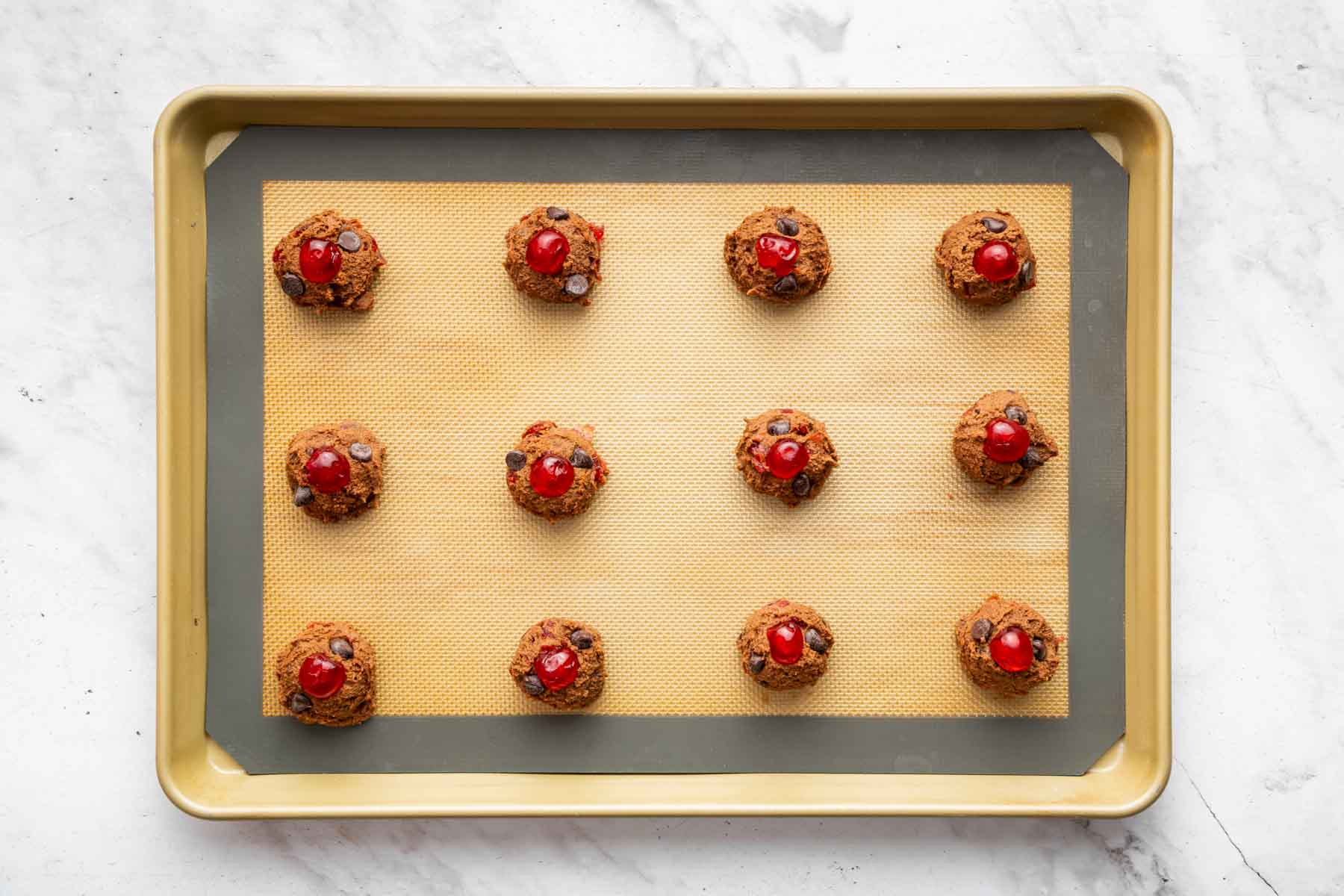 Twelve raw chocolate cherry cookie dough balls on a baking sheet.