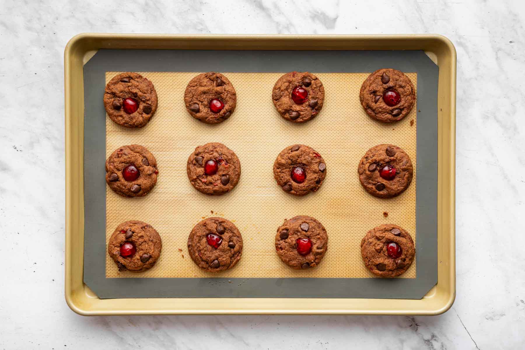 Twelve freshly baked brown cookies with red fruit bits on top.