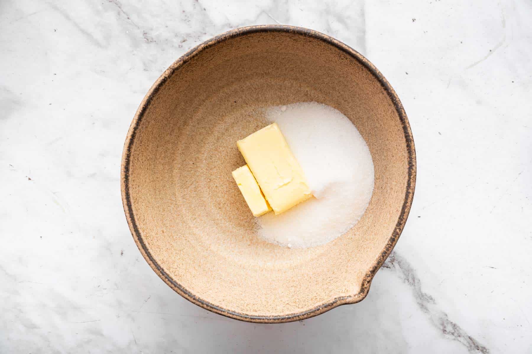 Brown baking bowl with granulated sugar and butter.