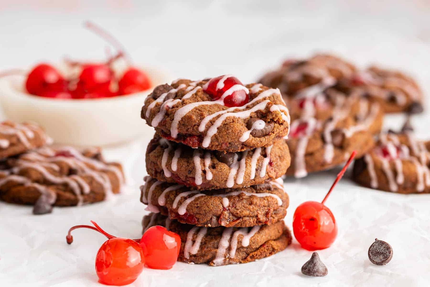 Stack of chocolate cherry cookies with maraschino cherries laying next to them.