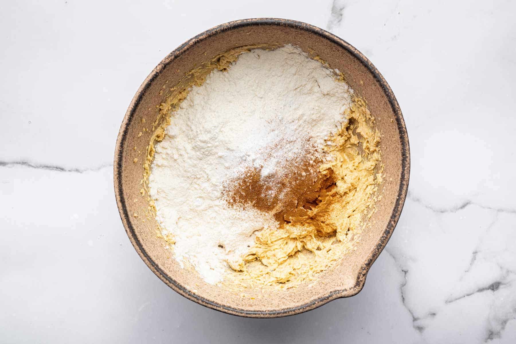 Brown dough in brown bowl with flour sprinkled on top.