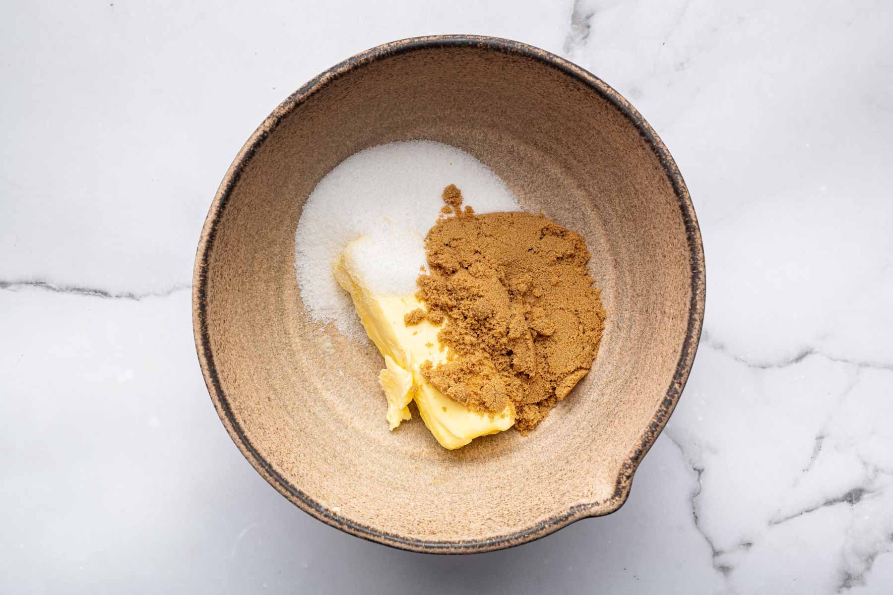 Brown bowl with butter and two types of sugar.