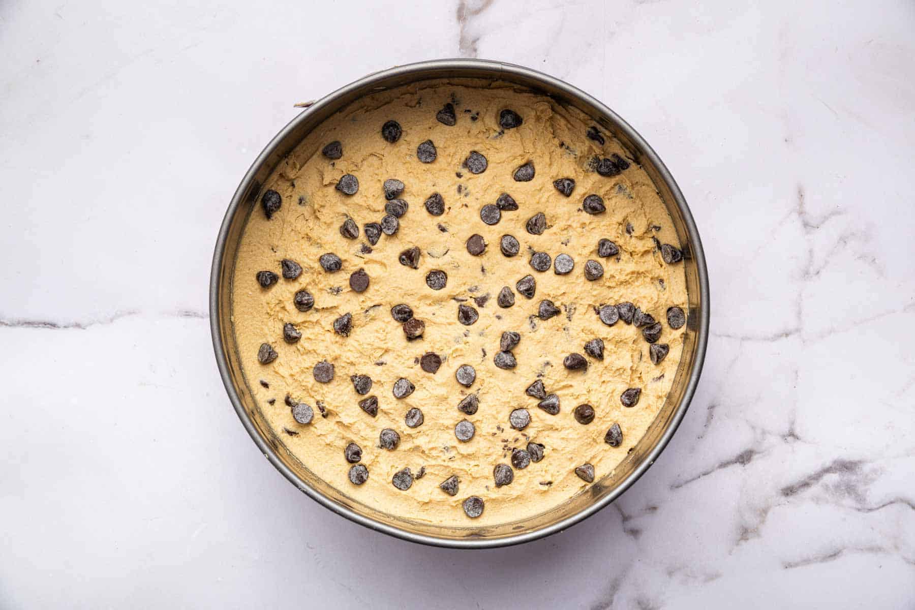 Raw cookie dough with extra chocolate chips on top in a 9-inch pan.