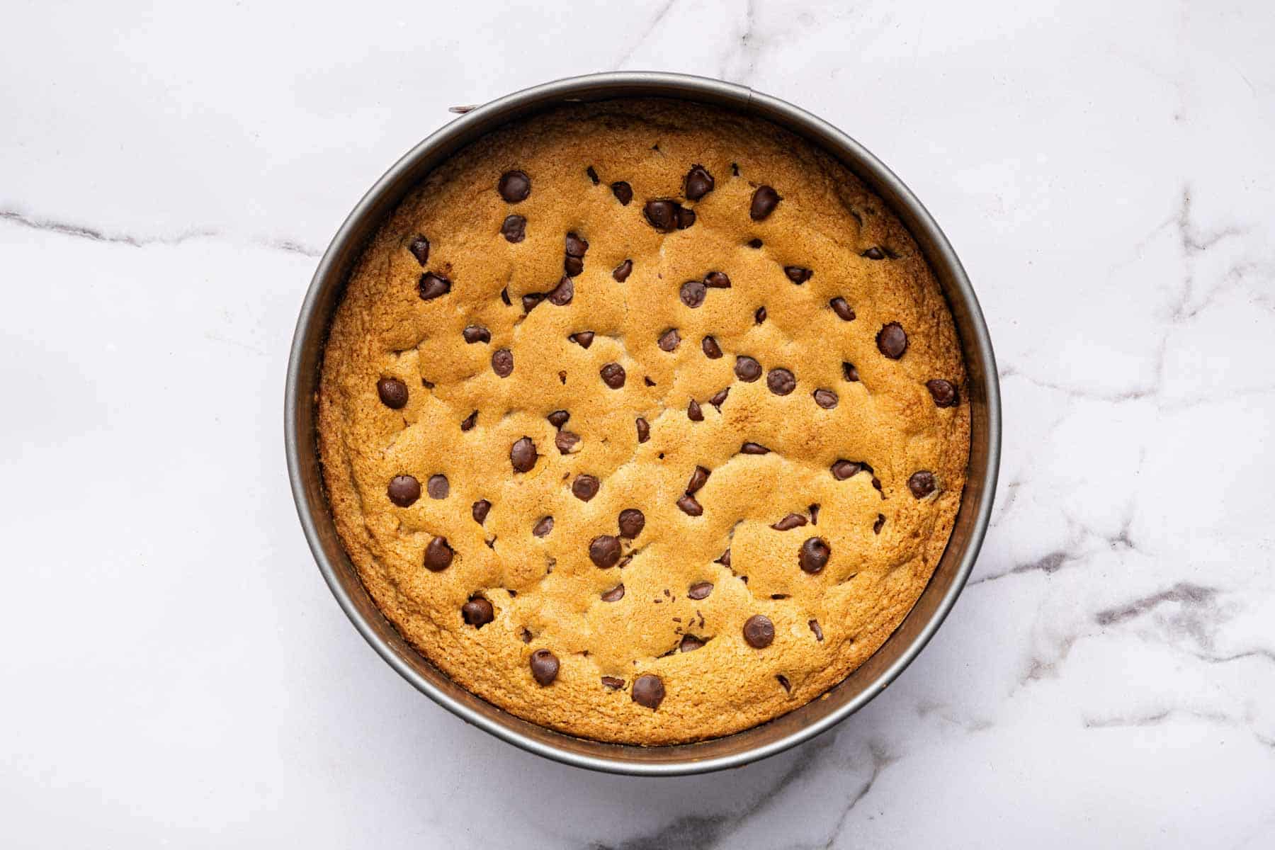 Freshly baked chocolate chip cookie cake in round cake pan.