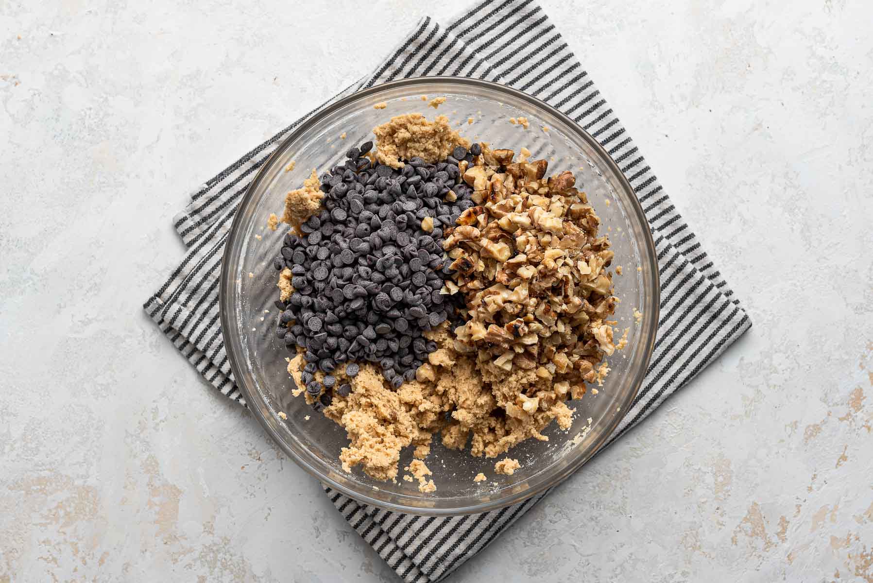 Chocolate chips and walnuts being added to cookie dough.
